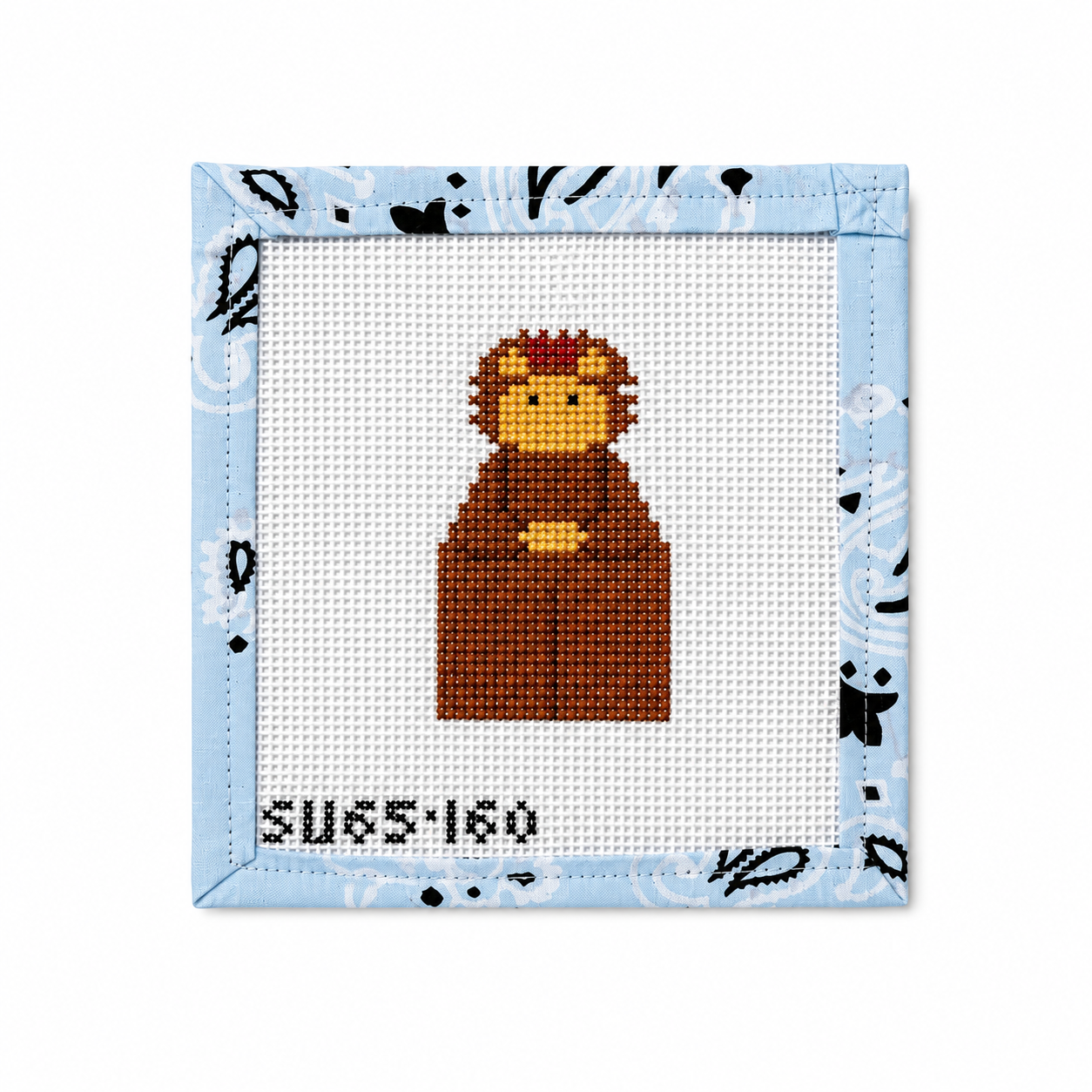 A square cross-stitch canvas featuring a pixelated brown bear holding a yellow ball, bordered by a light blue patterned fabric edge on a white background.